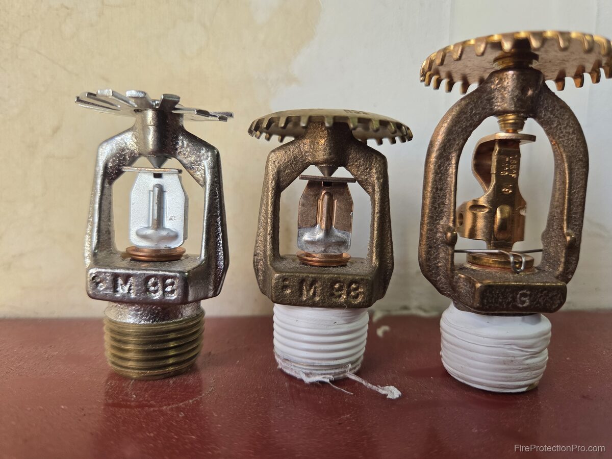Three upright fire sprinkler heads in different sizes showing glass bulbs and deflectors