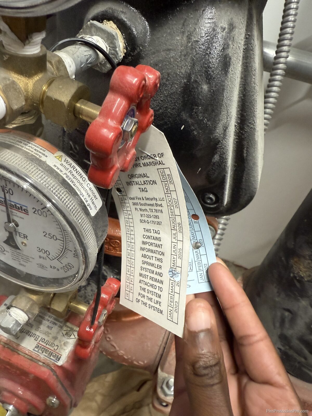 Inspection tag on sprinkler riser valve showing installation date and service details